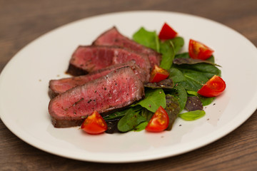 Juicy steak medium rare beef with green salad and tomatoes on white plate