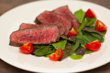 Juicy steak medium rare beef with green salad and tomatoes on white plate