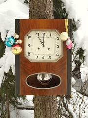 Clock decorated with Christmas toys in the winter forest on a fir covered with snow.