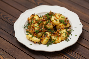 Gnocchi with a mushroom sauce and fresh herbs on a white plate, on a wood background