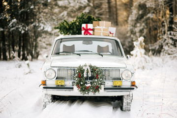 Retro car with gifts and Christmas tree in winter snowy forest and beautiful Christmas wreath. Holiday decor, Santa Claus delivery