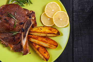 Grilled beef steak baked potatoes and lemon slices on green plate. Top view.