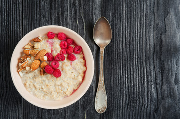Healthy and tasty breakfast. Fresh oatmeal with raspberries and bananas on dark wooden table. View from above. Copy space