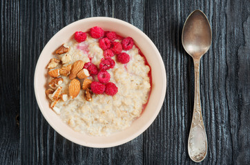 Fresh oatmeal with raspberries and nuts on dark wooden table. Healthy diet. Top view.