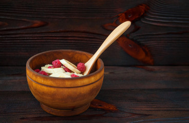 Natural oatmeal with banana and raspberries in a wooden bowl. Delicious and healthy breakfast.