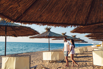 young couple in love holding hands among reed umbrellas on the sea beach.