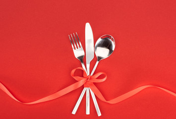 flat lay with fork, knife and spoon wrapped by red festive ribbon isolated on red, st valentine day...