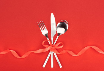 top view of  fork, knife and spoon wrapped by red festive ribbon isolated on red, st valentine day concept