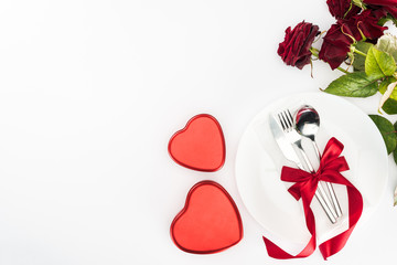 top view of plate and cutlery wrapped by festive ribbon, heart shaped present boxes and bouquet of red roses isolated on white, st valentine day concept