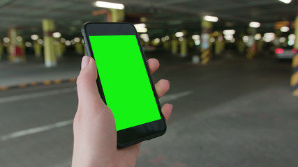 Lublin, Poland - July 2018: A hand holding a phone with a green screen in an underground parking lot. Close-up shot. Soft focus