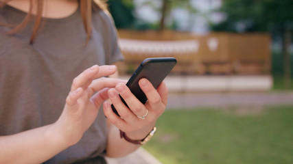 A close-up of a woman's hand holding and using a phone outdoors. Soft focus