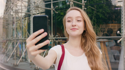 A happy smiling red-haired lady using a phone in the city street. Close-up shot. Soft focus