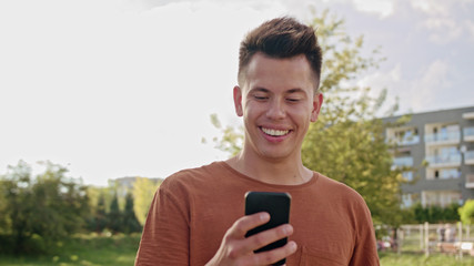 An attractive young man wearing an orange T-shirt using a phone in town. Close-up shot. Soft focus