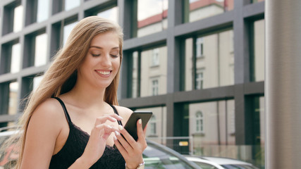 An attractive young lady using a phone in town while walking. Medium dolly shot. Soft focus