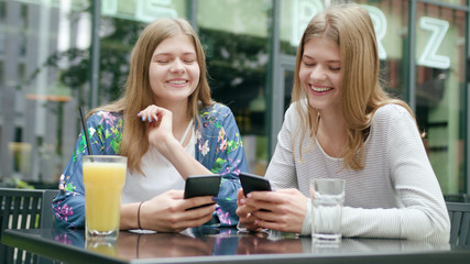 Attractive young ladies sitting at the table outdoors and using their phones. Medium shot. Soft focus