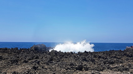 Sea water is beating against a rock of volcanic origin. Sunny day.
