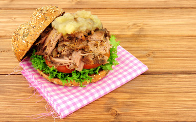 Hog roast meat sandwich with apple sauce and salad in a seed covered bread roll on a wooden background