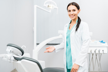 smiling female dentist showing chair in dental clinic