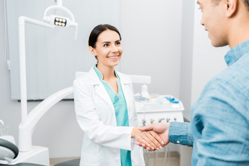 smiling female dentist shaking hands with  african american patient