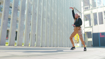 A young girl performs modern hip hop dance on the streets of the city during the summer, twisting and rotating.