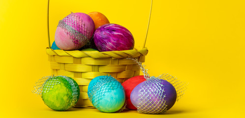 colorful, hand-painted, pastel Easter eggs in a basket on a bright, yellow, spring background
