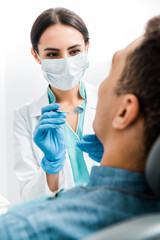 selective focus of female stomatologist in latex gloves and mask examining african american patient