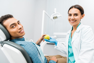 cheerful dentist giving apple to african american patient