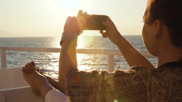Young woman enjoying sunrise on travel at sea. Taking pictures of the ocean on a ferry on cruise ship vacation