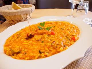 Closeup detail of a plate of seafood risotto next to a bread basket on a table at an Italian restaurant. Paris, France. Travel and cuisine.