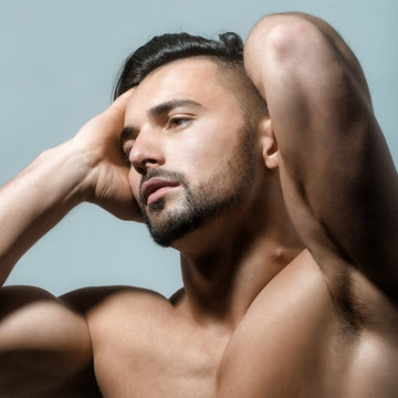 Portrait of handsome guy with strong muscular body on blue background. Fashionable trend in male's body and appearence. Brunette bodubuilder with modern beard and haircut. Striptease concept.