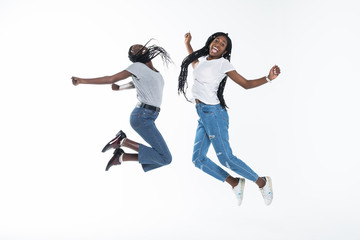 Two cheerful african girls jumping over white background