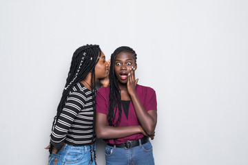 Portrait of two happy young african women sharing secrets isolated over white background