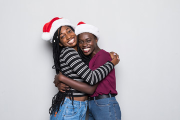 Portrait of young two african women with santa hats hugs isolated on gray background