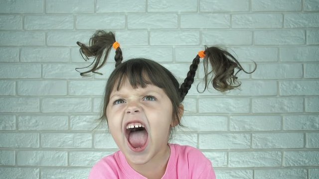 Portrait of a screaming little girl. A funny little girl screams, her hair rises from the scream.