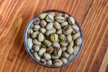 Pistachio nuts in a glass bowl on wooden background