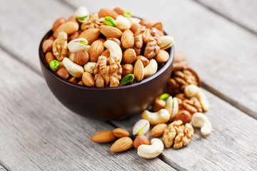 Wooden bowl with mixed nuts on a wooden gray background. Walnut, pistachios, almonds, hazelnuts and cashews, walnut.