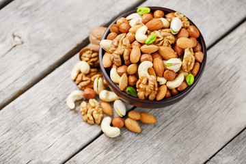 Wooden bowl with mixed nuts on a wooden gray background. Walnut, pistachios, almonds, hazelnuts and cashews, walnut.