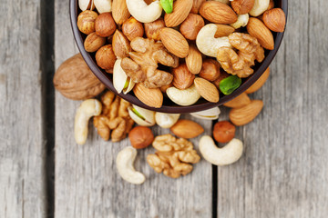 Wooden bowl with mixed nuts on a wooden gray background. Walnut, pistachios, almonds, hazelnuts and cashews, walnut.