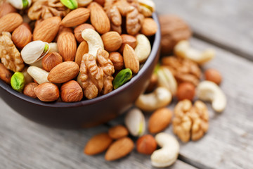 Wooden bowl with mixed nuts on a wooden gray background. Walnut, pistachios, almonds, hazelnuts and cashews, walnut.