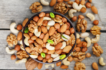 Wooden bowl with mixed nuts on a wooden gray background. Walnut, pistachios, almonds, hazelnuts and cashews, walnut.