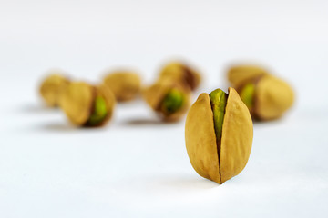 Single Salted roasted pistachio nut in front of other nuts on a white background