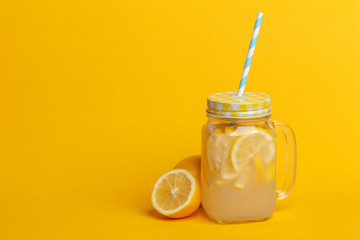 A jar of homemade lemonade and lemons on a yellow background.