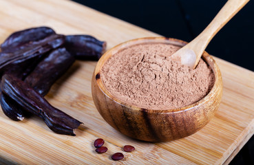 Carob pods and carob powder over wooden background