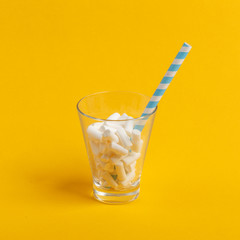 Glass cup with paper tube and marshmallows on a yellow background. Minimalistic concept.