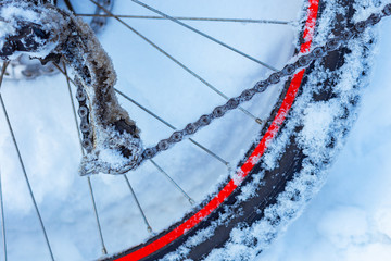 closeup of bicycle wheel with spokes, chain and transmission parts lying in snow partly covered. selective focus, shallow depth of field, all weather winter cycling, extreme outdoor