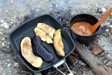 Cooking grilled eggplants in a cast-iron pan grill at the stake. Food tourists.