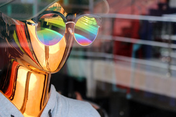 A reflective metallic gold mannequin wearing round sunglasses in a shop window
