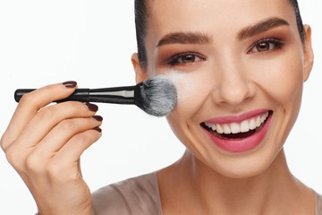 Portrait of a beautiful smiling young woman holding a brush in her hand and applying powder to her...