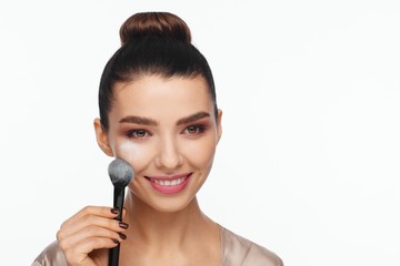 Portrait of a beautiful young woman holding a brush in her hand and applying powder to her face with a brush