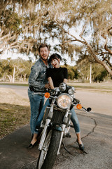 Fototapeta na wymiar Precious Cute Leisure Lifestyle Portrait of Handsome Guy and Girl Beauty Being Silly Fun and Laughing while Riding Classic Motorcycle Bike While in Love
